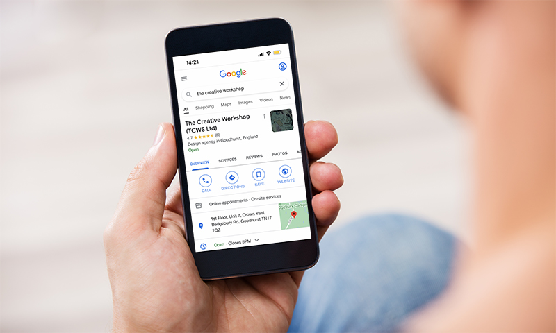 A photography of a man holding an iphone and viewing The Creative Workshop's Google My Business profile