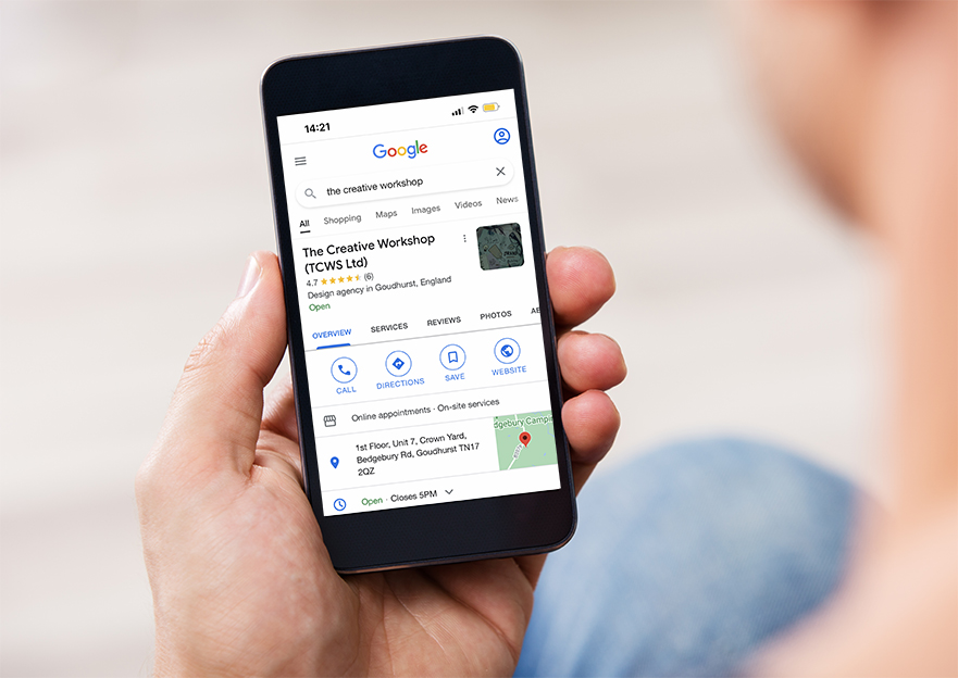 A photograph of a man holding an iphone and viewing The Creative Workshop's Google My Business profile on Google search..