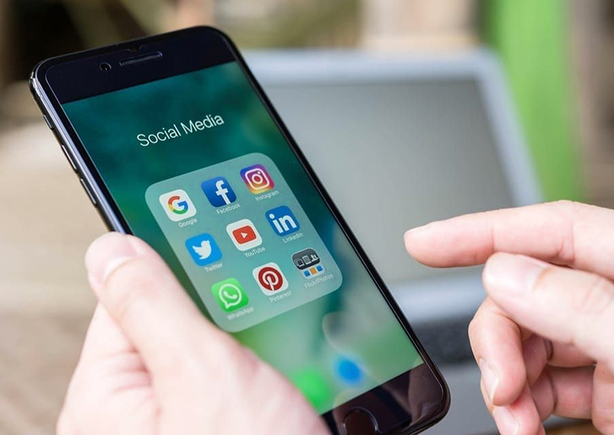 Photograph of a man holding an iphone and viewing the social media apps